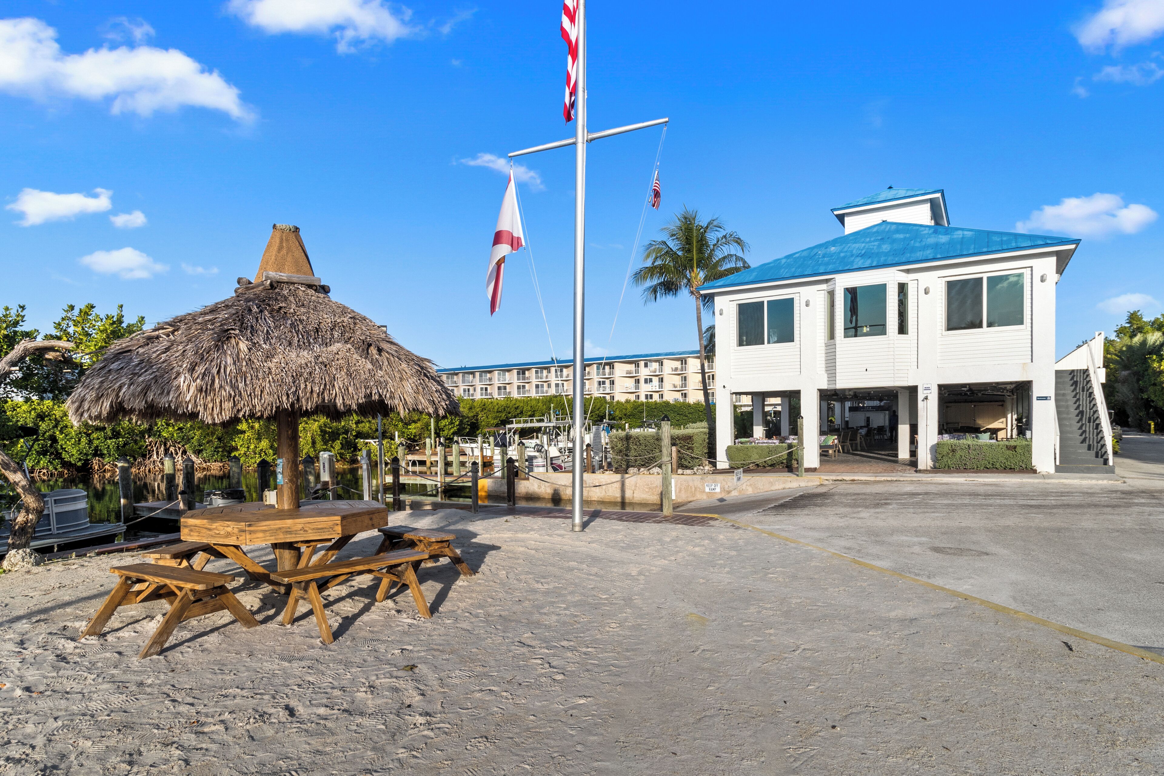 Ein Strandhotel mit einem Reetdachschirm, einem Holztisch und einer Fahnenmasten mit Flaggen.