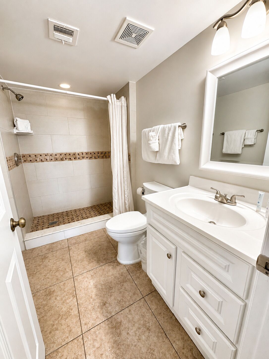 A bathroom with a shower, toilet, sink, and a mirror.