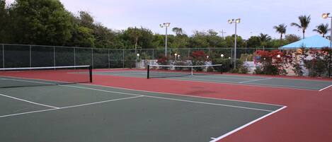 A tennis court with a net, surrounded by a fence and trees.