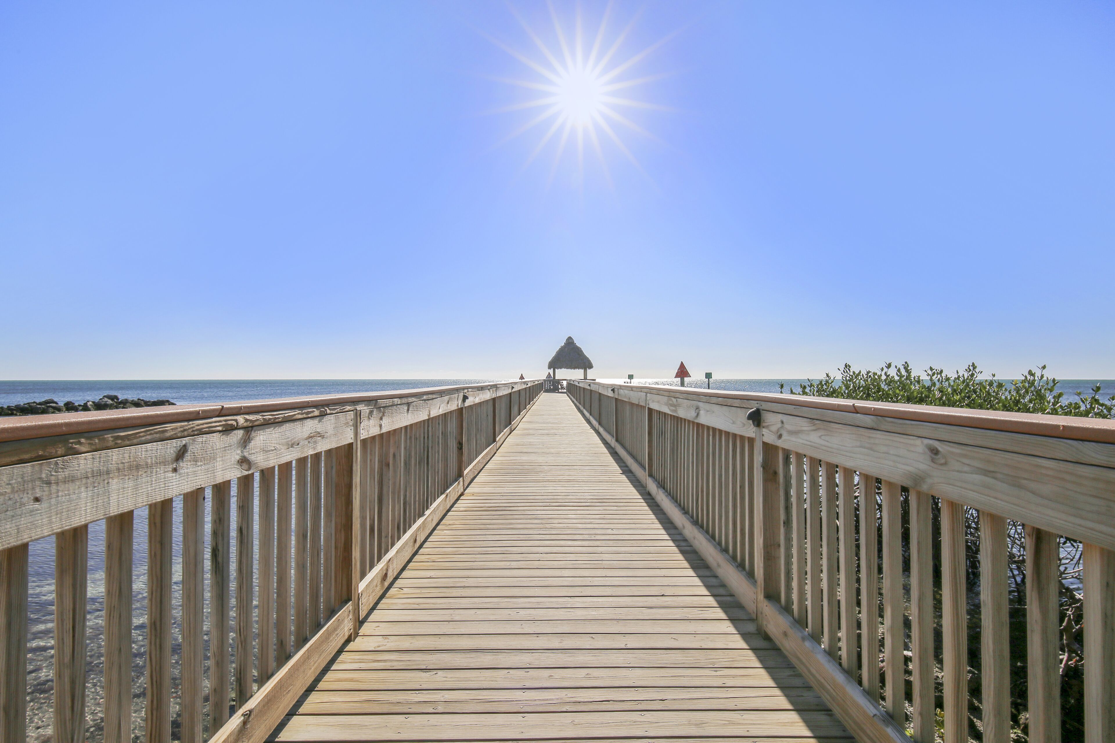 A wooden pier leading to a beach with a thatched-roof structure at the end.