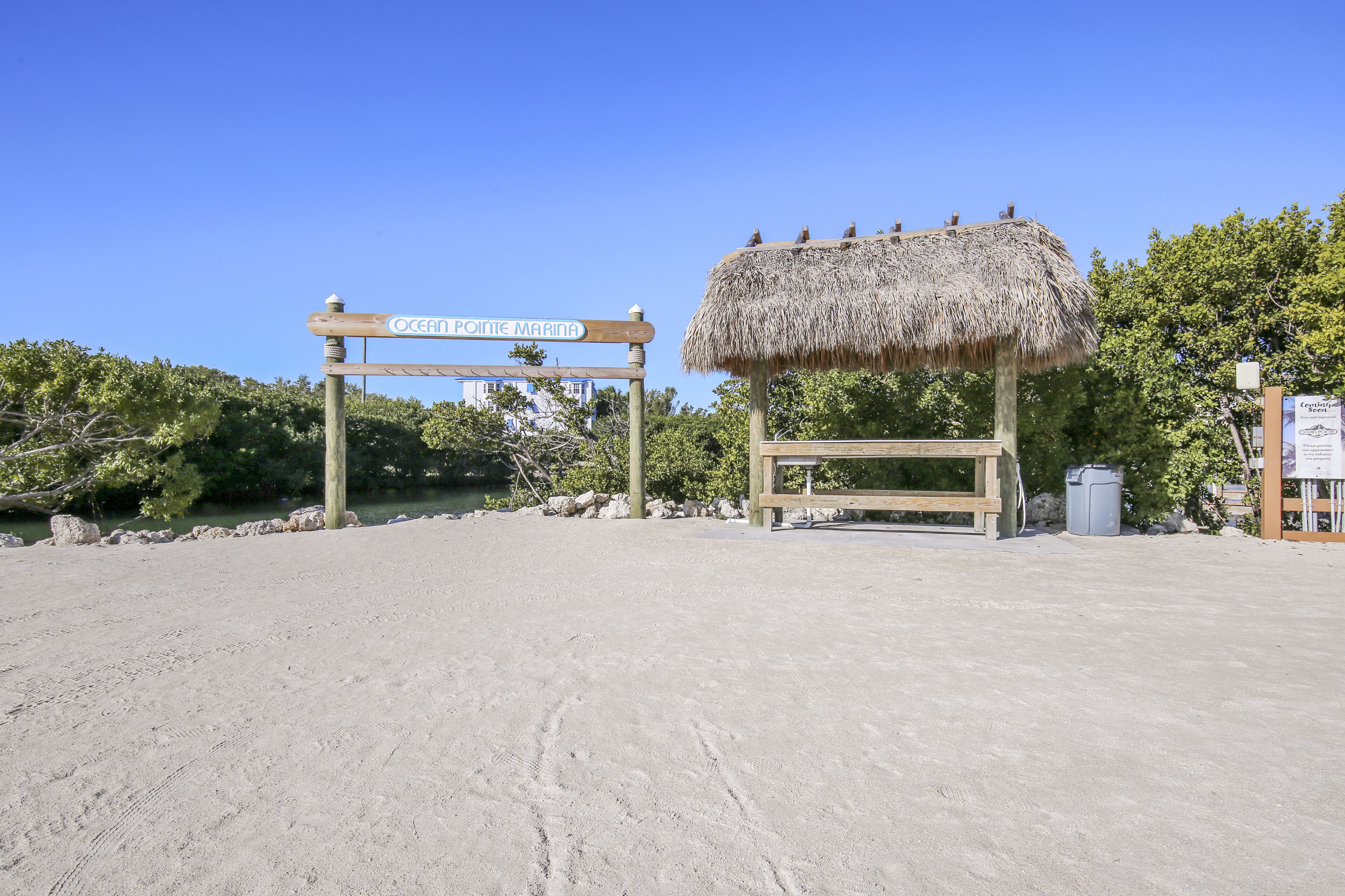 A beach entrance with a sign reading "Ocean Pointe Marina," a thatched structure, and a wooden bench.