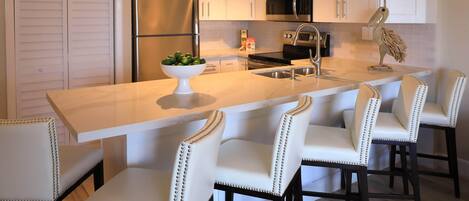 A modern kitchen with white cabinetry, a stainless steel refrigerator, a microwave, and a large island with bar stools.