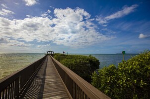 A wooden boardwalk leading to a gazebo by the water, surrounded by greenery.