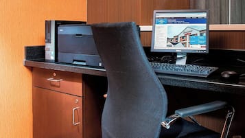 A hotel office with a desk, computer, printer, and a chair.