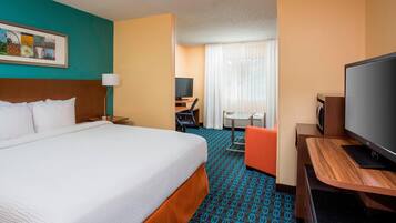 A hotel room with a large bed, a desk with a computer, a television, and a window with curtains.