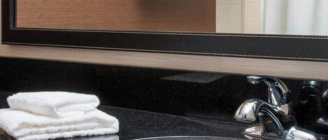 A bathroom with a black countertop, a white sink, and a mirror reflecting a towel rack with folded towels.