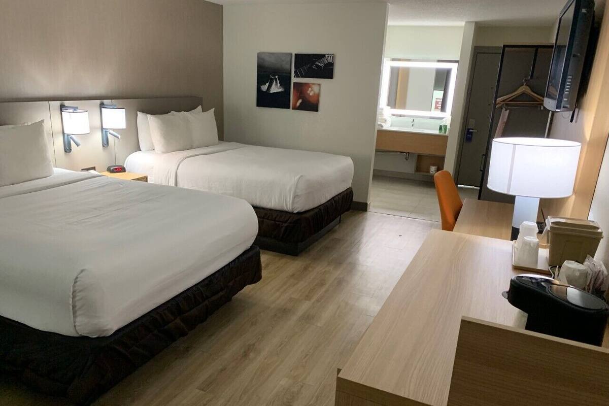 A hotel room with two beds, a desk, a chair, a TV, and a bathroom visible in the background.