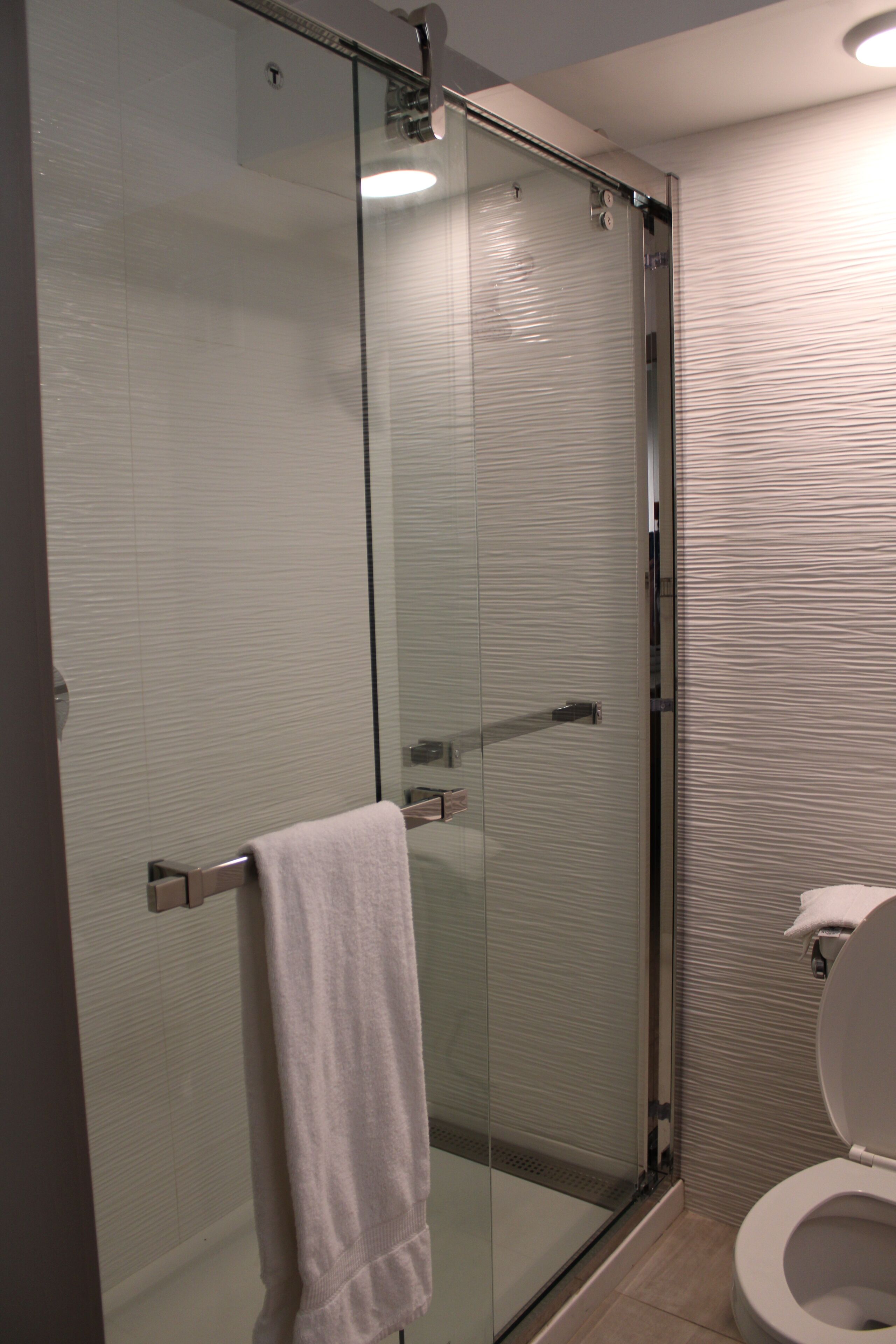 A modern bathroom with a glass shower enclosure, a white toilet, and a towel hanging on the shower door handle.