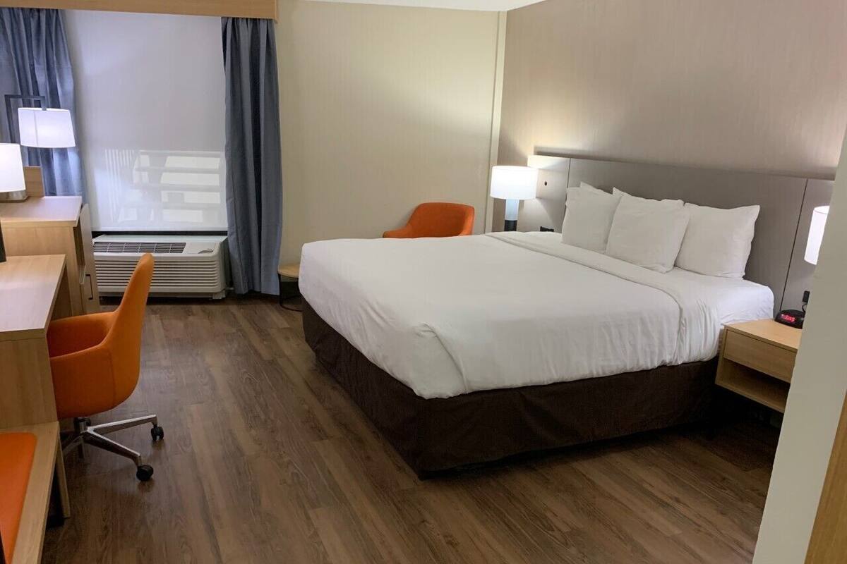 A hotel room with a large bed, two orange chairs, a desk, and a lamp.