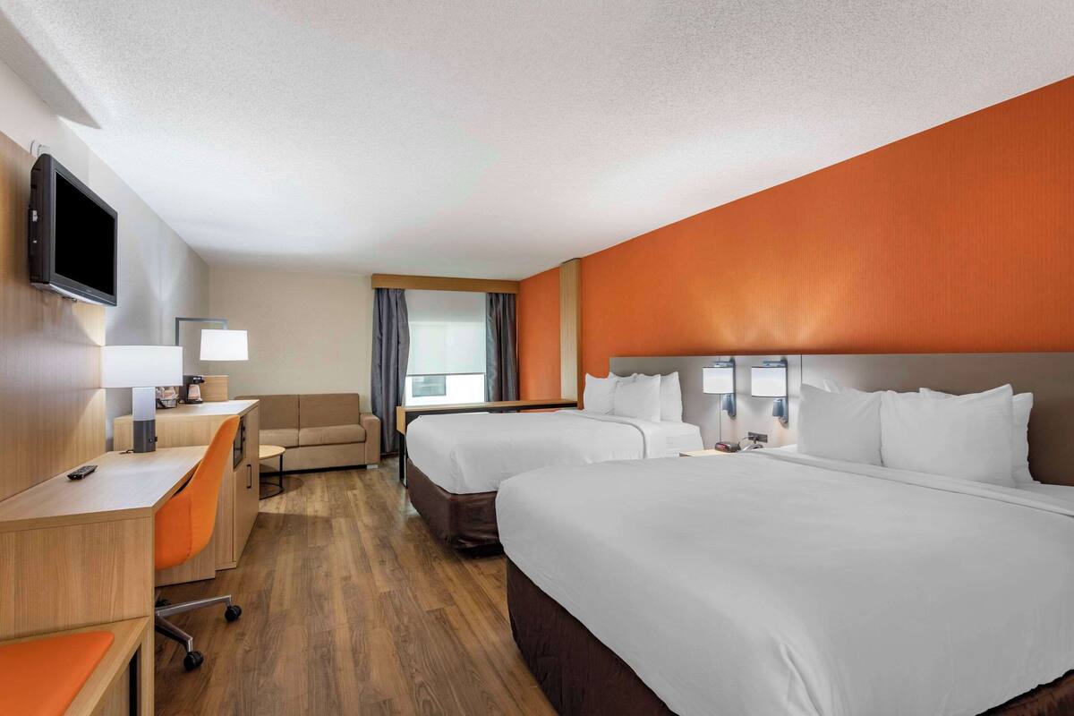 A hotel room with two beds, a desk, a chair, a TV, and a window with curtains.