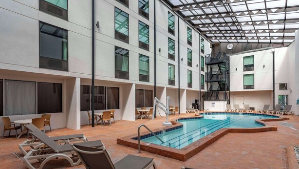 Una piscina interior con sillas y mesas de descanso, rodeada por un techo alto con tragaluces.