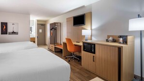 Habitación de hotel con dos camas, un escritorio con silla, televisor, lámpara y cafetera.