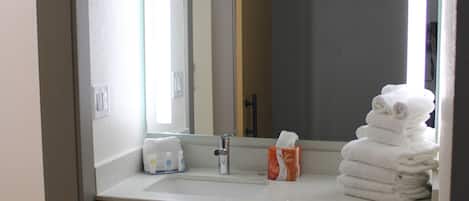 Une salle de bain avec un lavabo blanc, un miroir et une pile d’serviettes.
