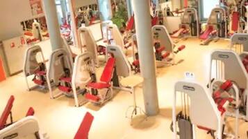 Un gimnasio con equipo de ejercicio, ventanas amplias y techo alto.