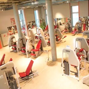 A gym with exercise equipment, large windows, and a high ceiling. - Nordsee Hotel Bremerhaven Fischereihafen (Bremerhaven)
