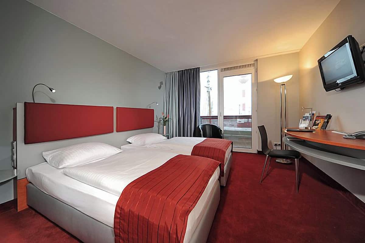 A hotel room with two beds, a desk, a chair, a television, and a window with curtains.