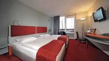 Una camera d'albergo con due letti, una scrivania, una sedia, una televisione e una finestra con tende.