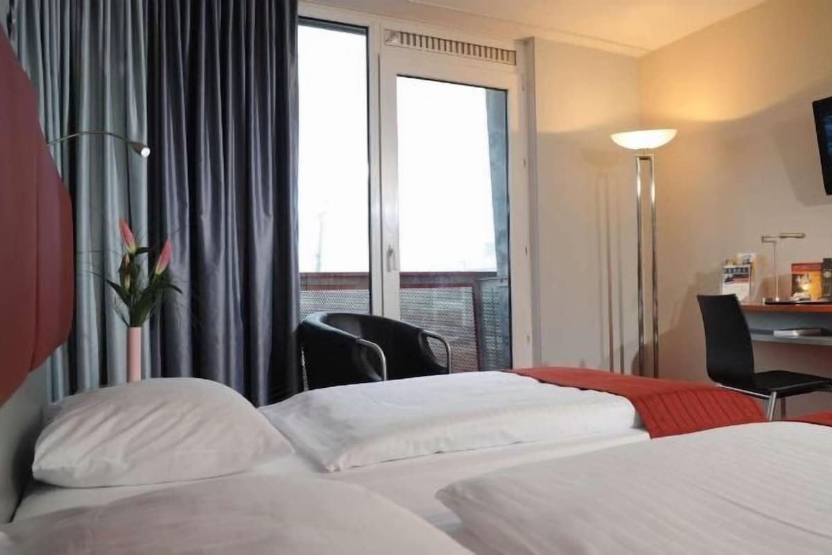 Une chambre d’hôtel avec un lit, un bureau, une chaise, une télévision et une fenêtre.