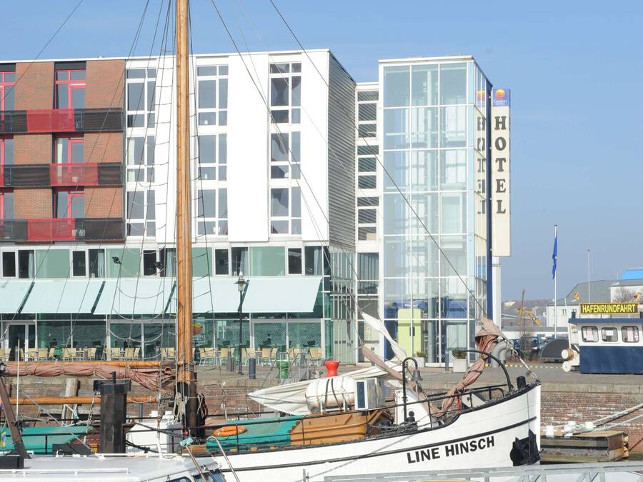 Un barco amarrado con letreros que dicen 'LINE HINSCH' y 'RESTAURANTE', un edificio con letreros de 'HOTEL', y un cielo azul despejado.