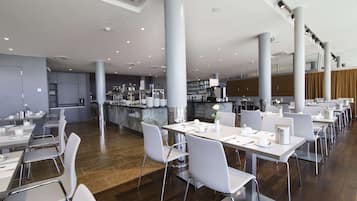 Un comedor amplio con mesas y sillas blancas, una barra central y una cocina al fondo.