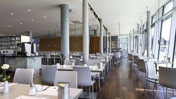 Et moderne spiseområde med lange borde, hvide stole og en marmor disk.