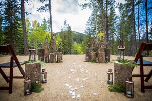 Decoración de boda en un bosque con sillas y faroles sobre tocones, dispuestos en círculo.