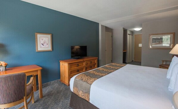 Una habitación de hotel con cama, escritorio, silla, televisor y cómoda.