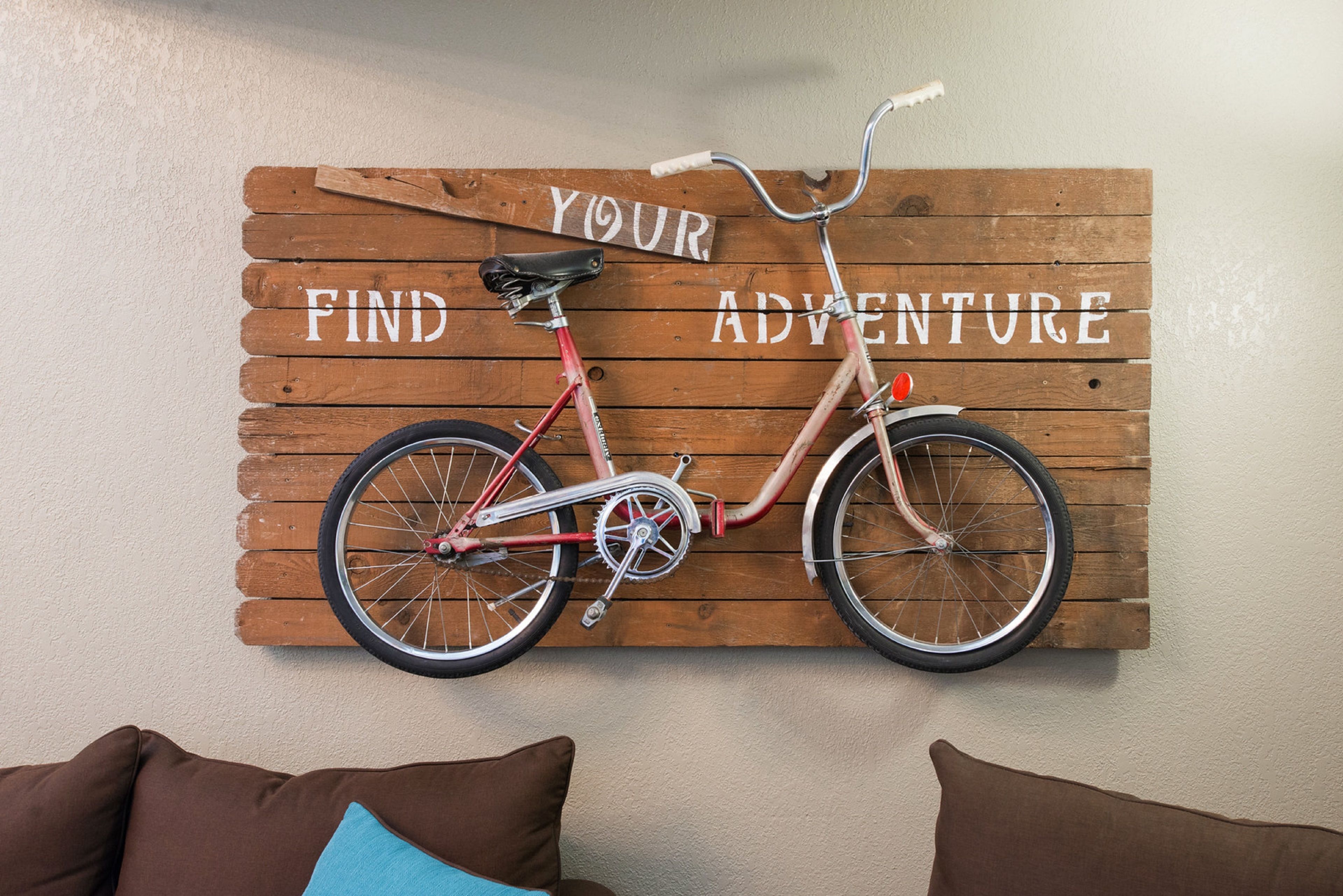 A wooden sign with a bicycle and the words "YOUR ADVENTURE" mounted on a wall.