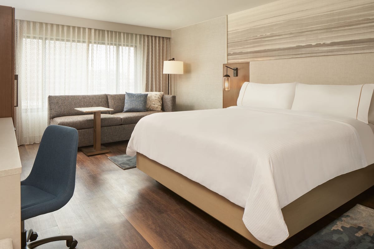 A hotel room with a large bed, a sofa, a desk, and a chair.