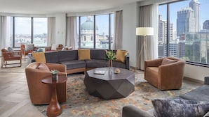 A modern living room with a sectional sofa, armchairs, a coffee table, and a floor lamp. Large windows offer a city view.