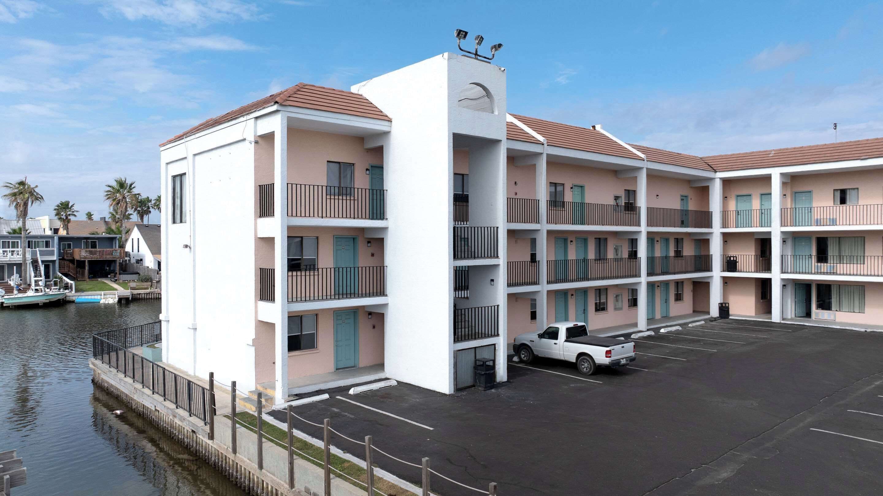 A multi-story hotel with balconies, a parking lot, and a dock with boats.