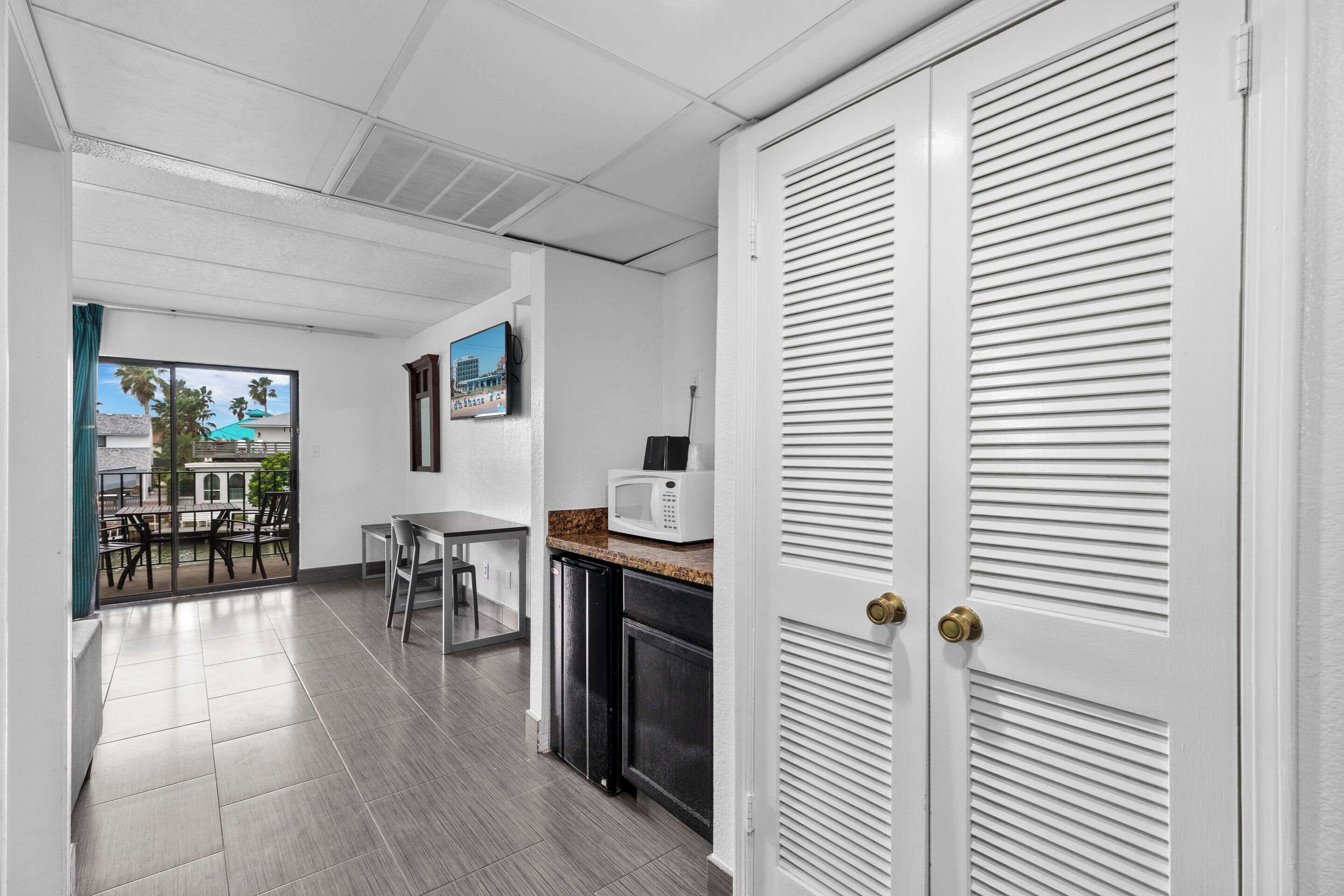 A modern kitchen with a microwave, a dining table, and chairs. There is a sliding door with a view of the outside.