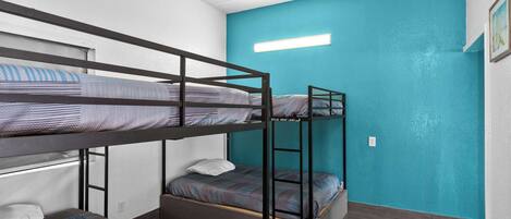 A bunk bed room with a teal accent wall and a small window.