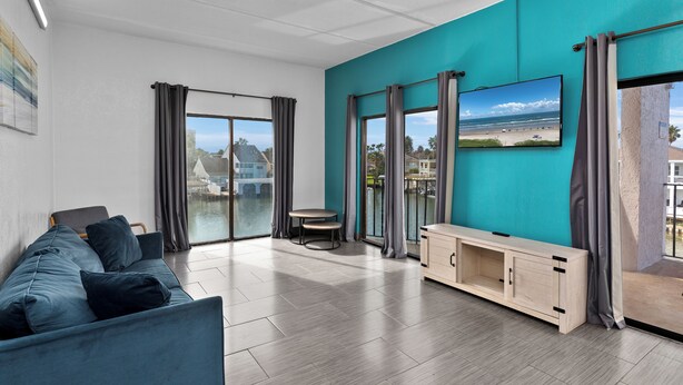 Una sala de estar moderna con una pared de acento color turquesa, un sofá, un televisor y vistas a la playa.