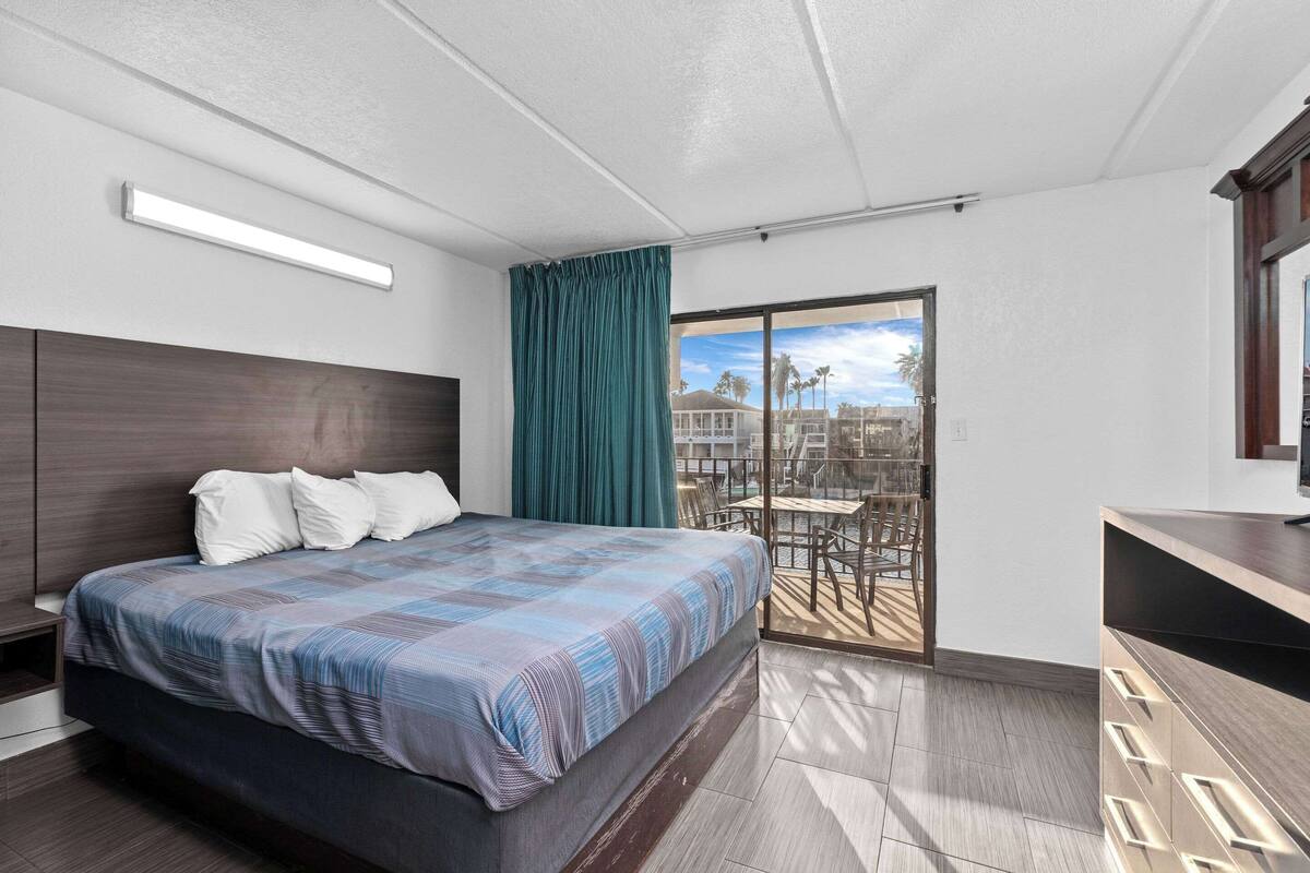 A modern hotel room with a large bed, a desk, and a balcony with outdoor seating.