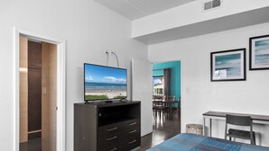 Una habitación de hotel moderna con una cama grande, un televisor de pantalla plana sobre un mueble de madera, un escritorio con una silla y una zona de comedor con mesa y sillas.