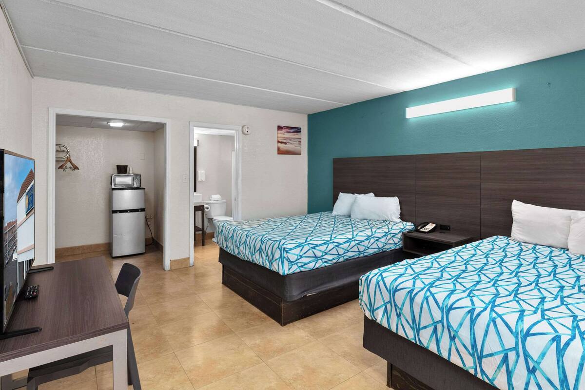 A hotel room with two beds, a desk, a refrigerator, and a TV.
