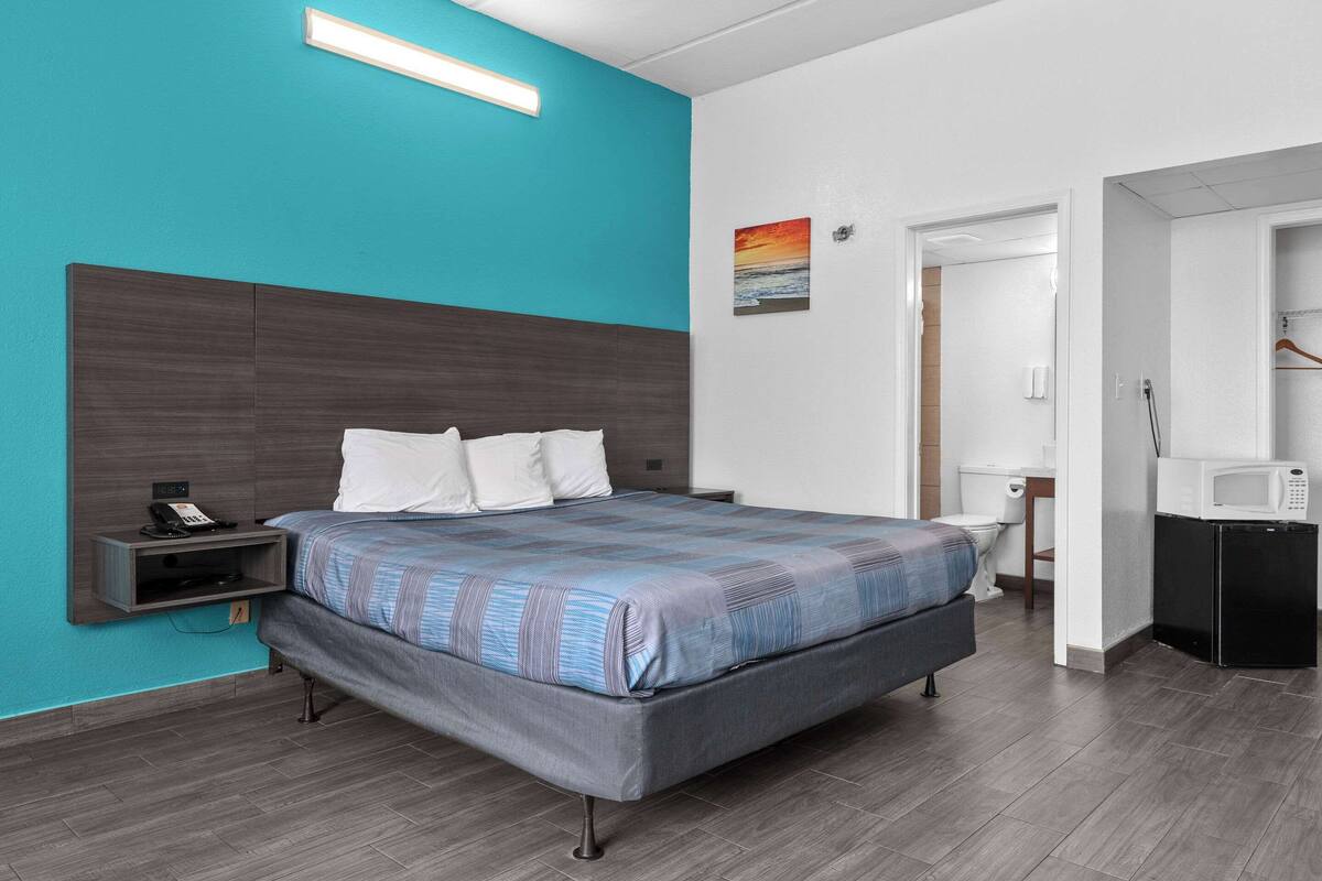 A modern hotel room with a large bed, a bedside table with a phone, a microwave, and a small refrigerator.