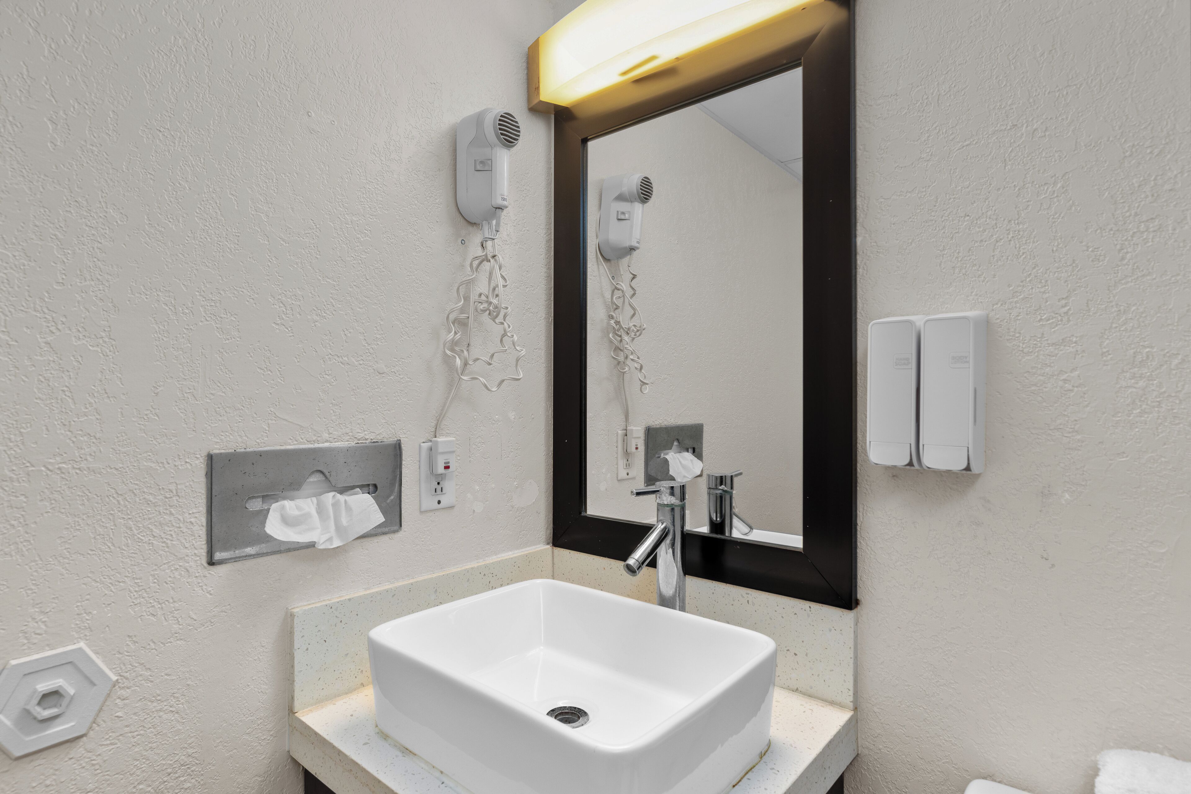 A bathroom with a white sink, a mirror with a black frame, and a hairdryer mounted on the wall.
