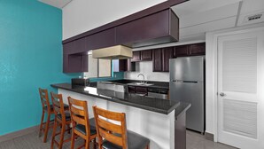 Una cocina moderna con una isla central, taburetes de bar, armarios de madera oscura y un refrigerador de acero inoxidable.