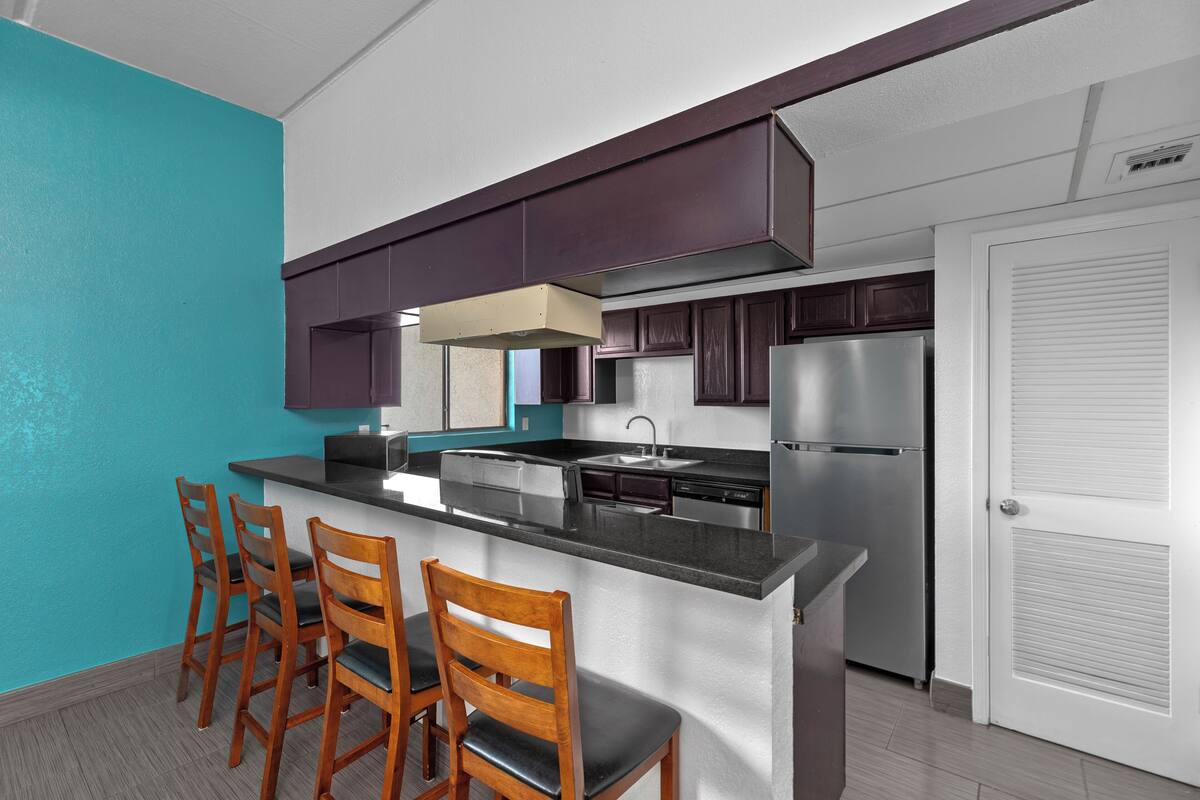 A modern kitchen with a central island, bar stools, dark wooden cabinets, and a stainless steel refrigerator.