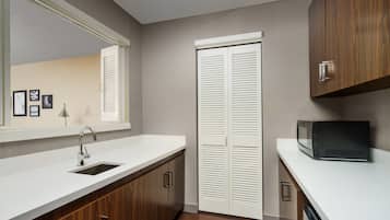 A modern kitchen with a white countertop, a stainless steel sink, wooden cabinets, a microwave, and a white door with louvered panels.