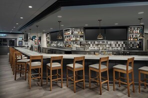 A bar area with wooden bar stools, a counter with bottles, and pendant lighting. - Four Points by Sheraton Pleasanton (Pleasanton)