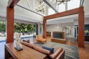 A spacious living area with a wooden coffee table, leather sofa, and a TV. - Four Points by Sheraton Pleasanton (Pleasanton)