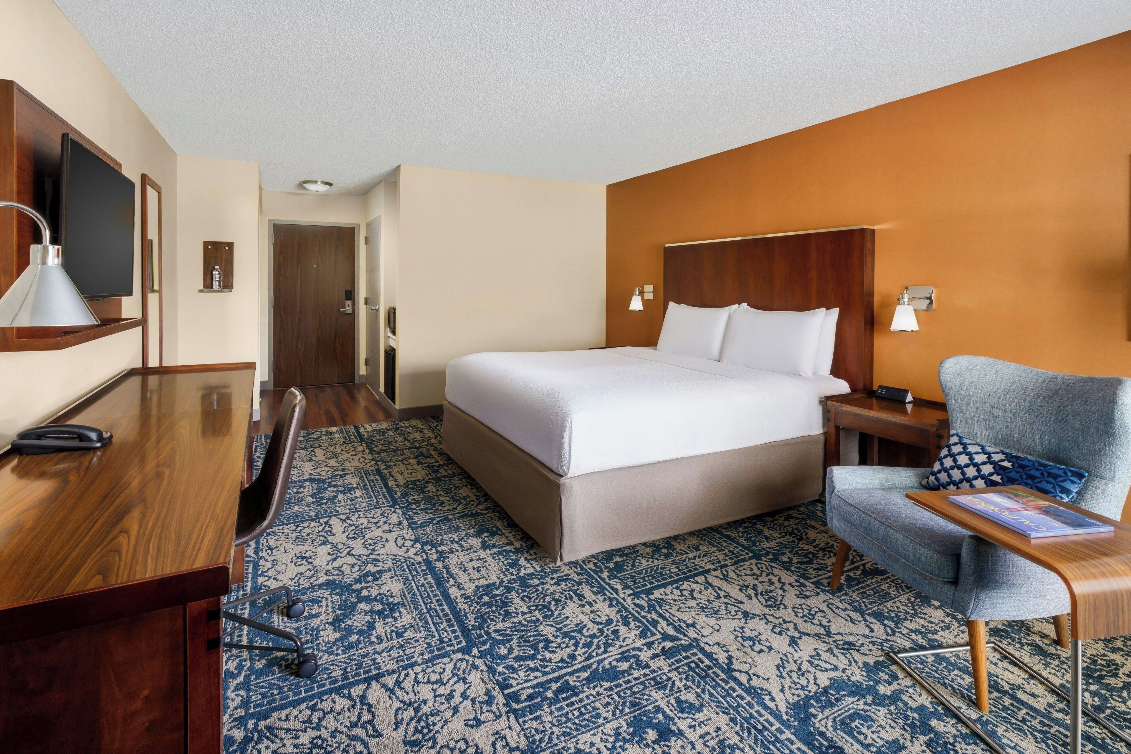 A hotel room with a bed, desk, chair, and a television.