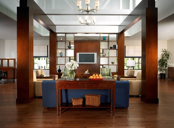 A spacious living area with a blue sofa, wooden coffee table, and a TV on a wooden wall. There are wicker baskets on the table and a potted plant in the corner. - Four Points by Sheraton Pleasanton (Pleasanton)