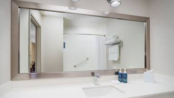 Un baño moderno con un espejo grande, un lavamanos y dos botellas de artículos de aseo.