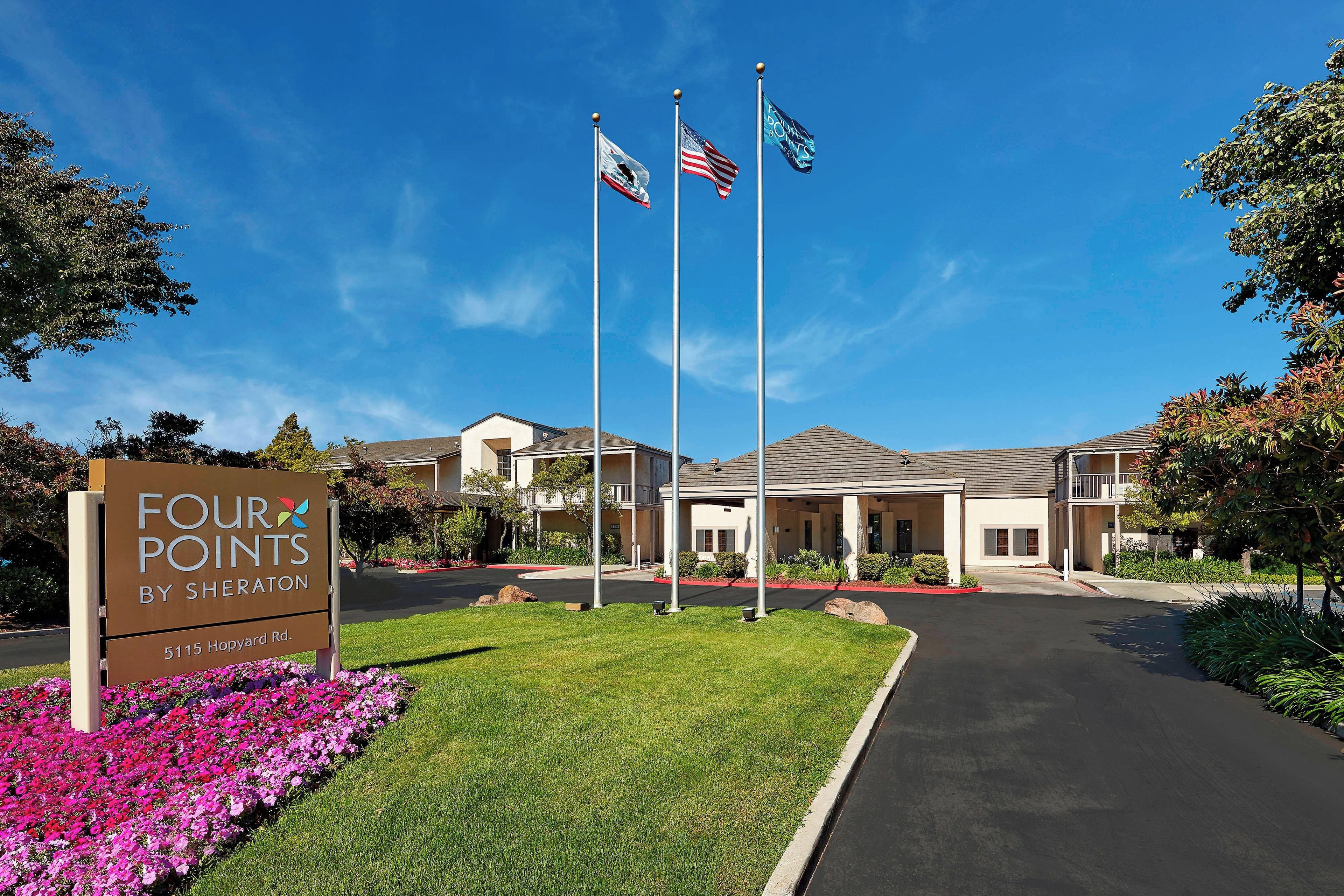 A residential complex named 'Four Points by Sheraton' with a clear sky, a well-maintained lawn, and a driveway leading to the entrance.