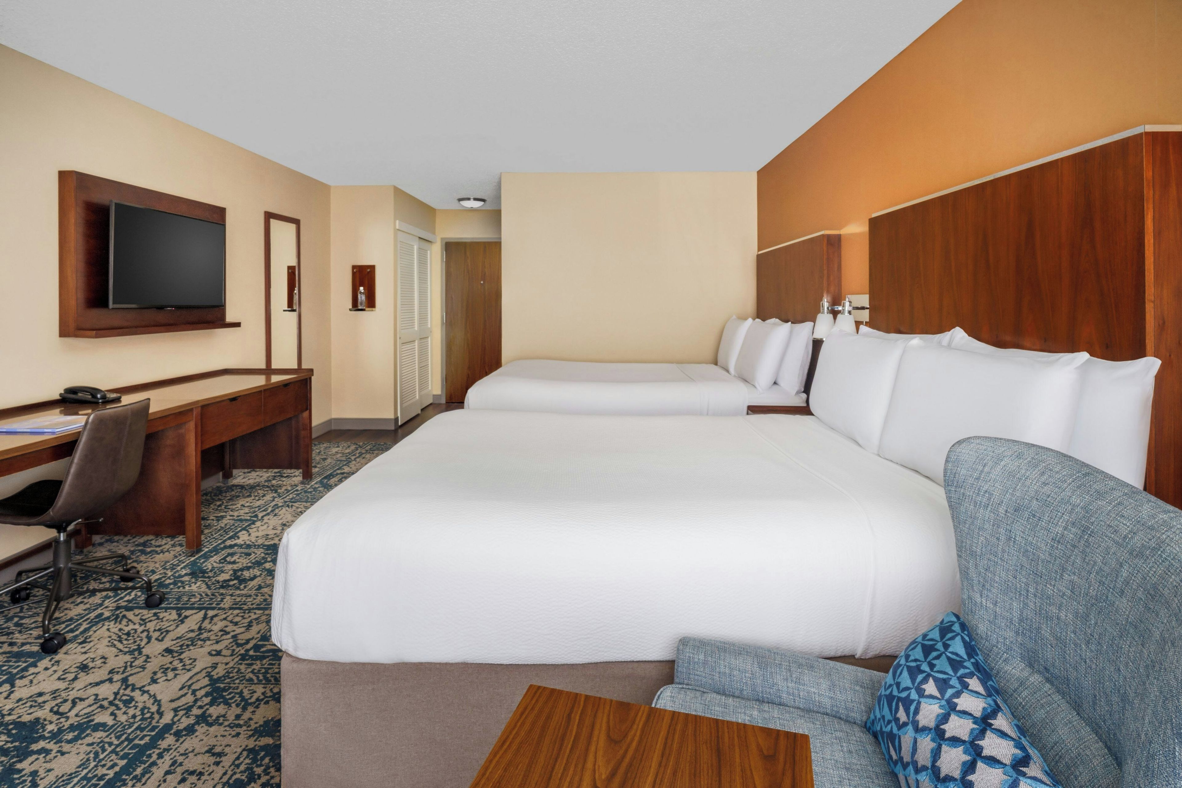 A hotel room with two beds, a desk, a chair, a television, and a small table.