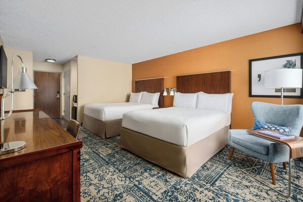 A hotel room with two beds, a desk, a chair, and a patterned carpet.